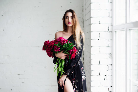 Portrait of beautiful brunette girl with red peonies. Happy boho woman portrait with peony flowers. Creative floral photo.