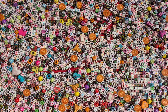 small white and black cubes with holes and the English alphabet lie on the red surface of the table, multicolored letters. rough texture