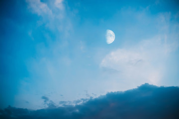 Naklejka na ściany i meble Cloudy blue sky with rising moon in the evening sky.