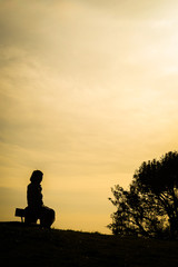 Obraz na płótnie Canvas 夕焼けの丘に座る女性のシルエット