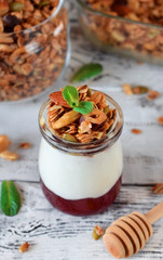 Layered breakfast with granola, yogurt and jam in a glass jar on the white table