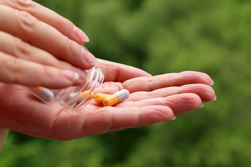 Woman with pills, female hands with a bottle of tablets in capsules on blurred green nature background. Concept of vitamins for beauty, diet pill, health care, natural drug