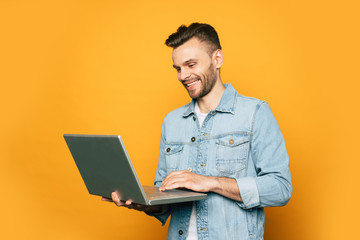 Modern young student or business man is working with laptop in hands on yellow background
