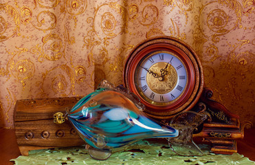 Photo of an old clock, casket and glass fish on brown background