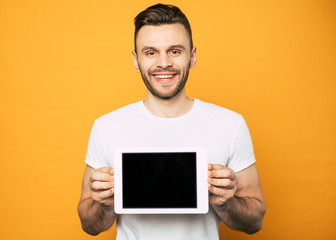 Handsome young man is showing blank screen of tablet in his hands on camera and smiling