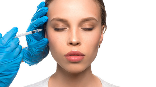 Close up of medical doctor in blue gloves injecting woman in the face with a suringe