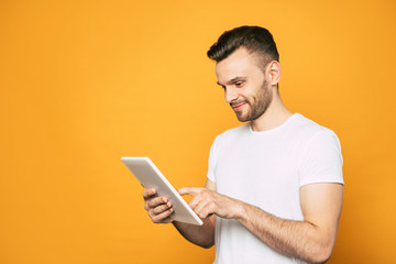 Side view portrait of casual business man with modern tablet in hands over yellow background