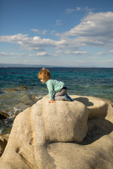 Child on the rocks by the sea. Summer holidays. Mountaineering. Rock climbing. Brave boy. Freedom. Childrens energy.