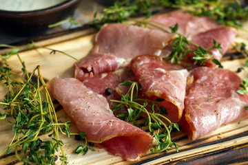 delicious pork bacon sliced ​​into strips on a wooden background with spices and fresh thyme. A serving of low-fat succulent farm meat pork. Food Photography