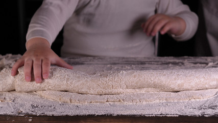 A little boy on a black background helps his father (dad) chef, preparing the dough to roll out for the pizza buns bread cakes and various flour products. Concept of: Little Chef, Baker, Slow motion.