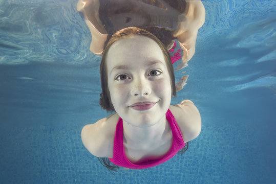 Portrait of a smiling teen girl in pink swimsuit smims underwater in a swimming pool