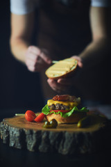 The cook adds the sauce to the burger, creates the final touch.A recipe for cooking, making a juicy hamburger, a menu, homemade recipes. Vertical photos