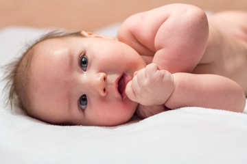 Newborn baby lying on its side and smiling on a white sheet and looking up