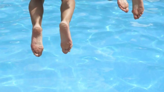 Two girls in bikini holding hands and jumping in the swimming pool in slow motion