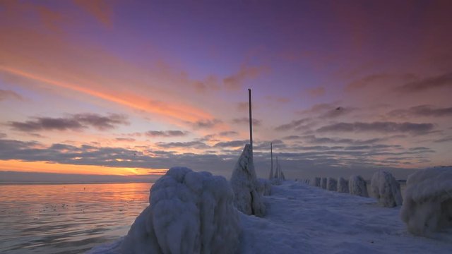 Unusual frozen pier and ocean at beautiful sunrise light with flying seagulls