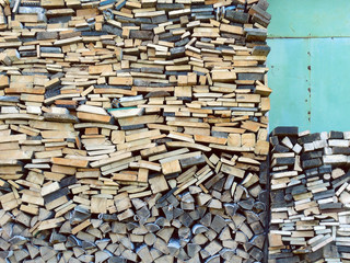 Firewood stacked in a woodpile near the green wall of the barn. Preparing for the winter