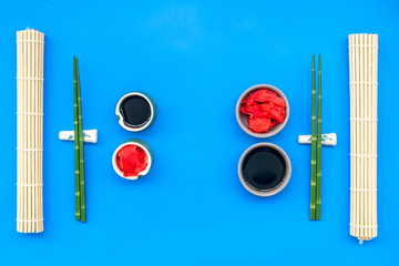 oriental table set up with bamboo sticks for sushi and maki, soy sauce on blue background top view