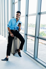 Businessman sitting on luggage and happy smiling using smartphone for business while travelling