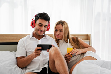 Couple caucasian lover enjoy music video on social media online with smartphone while sitting on bed in morning