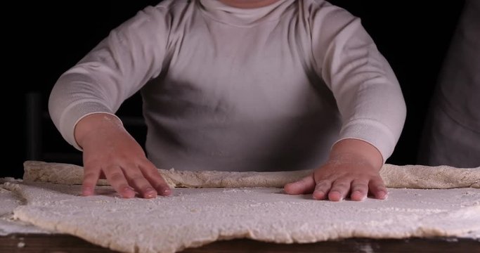 A little boy on a black background helps his father (dad) chef, preparing the dough to roll out for the pizza buns bread cakes and various flour products. Concept of: Little Chef, Baker, Slow motion.