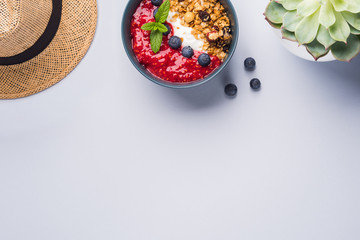 Yogurt smoothie bowl with blended raspberries, blueberries and oat matcha granola on pastel background. Delicious healthy breakfast concept