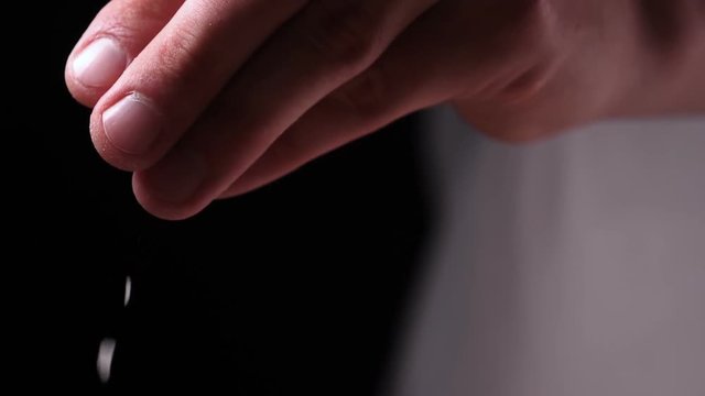 In slow motion on a black background, salt (flour) is strewed from one hand. Concept of: Time, Kitchen, Life, Hand, Crystal, Crystal Salt.
