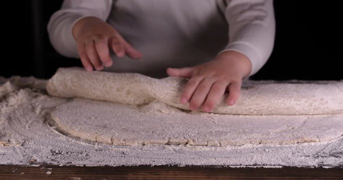 A little boy on a black background helps his father (dad) chef, preparing the dough to roll out for the pizza buns bread cakes and various flour products. Concept of: Little Chef, Baker, Slow motion.