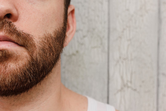 Close up portrait of bearded half men's face over wooden background young man shaves beard with trimmer or electric shaver at home