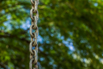 Obraz premium iron chain hanging on a green blurred unfocused background, industry and ecology connection concept pattern picture with empty copy space for text or inscription 