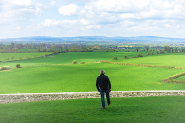 Fototapeta premium Middle-aged man walking in the field about to jump a wall, a stone fence. Overcome difficulties. Walk facing towards.