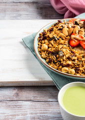 Delicious amaranth porridge topped with home made granola, strawberries and almond butter. Vegan plant based breakfast served with matcha latte on white wooden board. Healthy colorful food concept