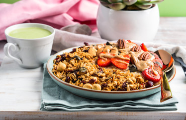 Delicious amaranth porridge topped with home made granola, strawberries and almond butter. Vegan plant based breakfast served with matcha latte on white wooden board. Healthy colorful food concept