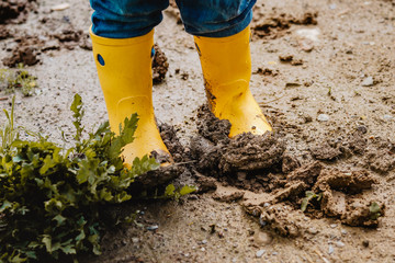 Child legs in yellow muddy rubber boots on wet mud.  Baby playing with dirt at rainy weather....