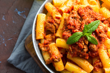 Delicious rigatoni pasta with italian tomato meat ragu sauce served in a pan on dark brown background. Traditional pasta dish concept. Home made lunch