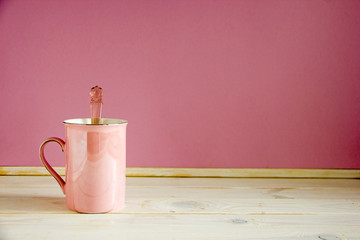 One pink cup with a handle on a pink background, in it a teaspoon.Mug stands on a wooden table. Copy space.