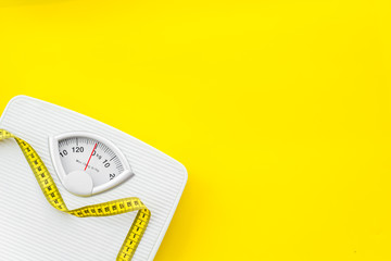bathroom scales and measuring tape for weight loss concept on yellow background top view mock up