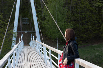 A young woman in a red dress and black leather jacket stands on a wooden bridge, clawing at the...
