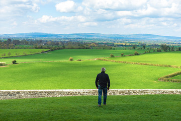 Middle-aged man walking in the field about to jump a wall, a stone fence. Overcome difficulties. Walk facing towards.