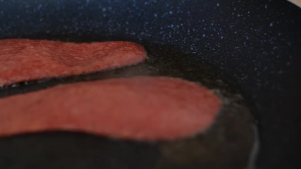 A panning shot from left to right of two ration of Quorn veggie & vegan bacon sizzling in a hot frying pan full of sizzling oil, a great breakfast supplement for national vegetarian week.