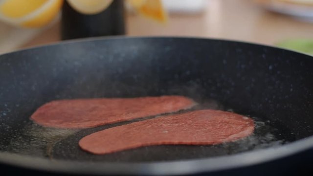 A panning shot from left to right of a ration of Quorn veggie & vegan bacon being put into a hot frying pan full of sizzling oil, a great breakfast supplement for national vegetarian week.