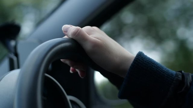 Close up of a female hand on a car steering wheel driving through a suburb in the middle of the day. A joyful drive through the town with greenery and nice houses in the background