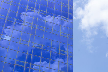Blue windows of a building with clouds reflected in them against a cloudy sky