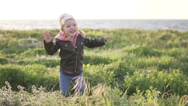 A little girl walks by the sea. She jumps up and laughs. happy baby in spring at sea. Walk in the park deserted wild park by the ocean