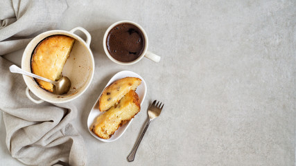 Pan with cottage cheese casserole, slices of casseroles in a plate and cup of coffee on gray table