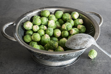 raw Fresh organic Brussels sprouts in metal colander on grey kitchen dresser.