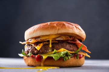 Tasty grilled beef burger with fried bacon and eggs, cheese, tomatoes and lettuce. - obrazy, fototapety, plakaty