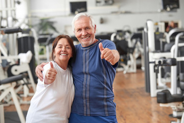 Fototapeta na wymiar Senior couple giving thumbs up at gym. Happy couple of seniors gesturing thumbs up at fitness center. People and healthy lifestyle concept.