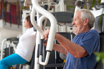 Senior man training on machine at fitness center. High-intensity workouts for senior people. Sport...