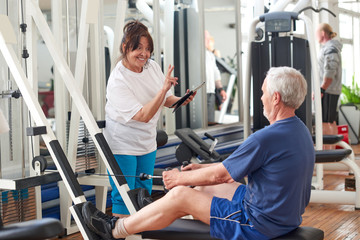 Senior people exercising at gym. Elderly woman using digital tablet at fitness club. People, sport, modern technology and lifestyle concept.