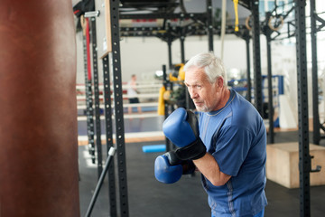 Senior male boxer ready to fight. Senior boxer in gloves boxing in gym.
